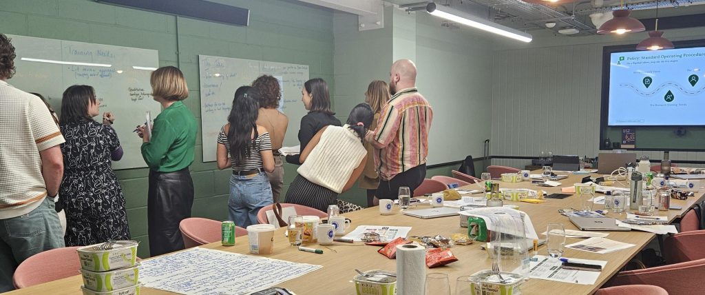 A group of people in a training room writing on aa whiteboard.